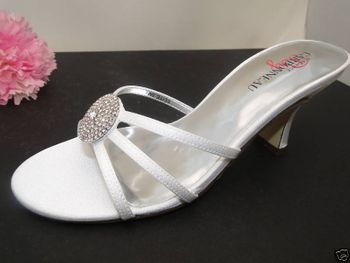 Silver sandal with a decorative buckle on a black surface with a pink flower.